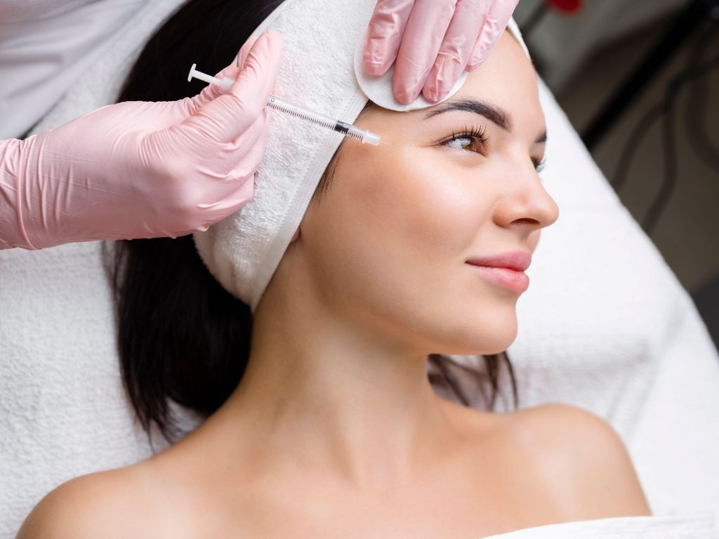 Woman on a treatment bed receiving a facial injectable treatment from a doctor in a professional medical setting