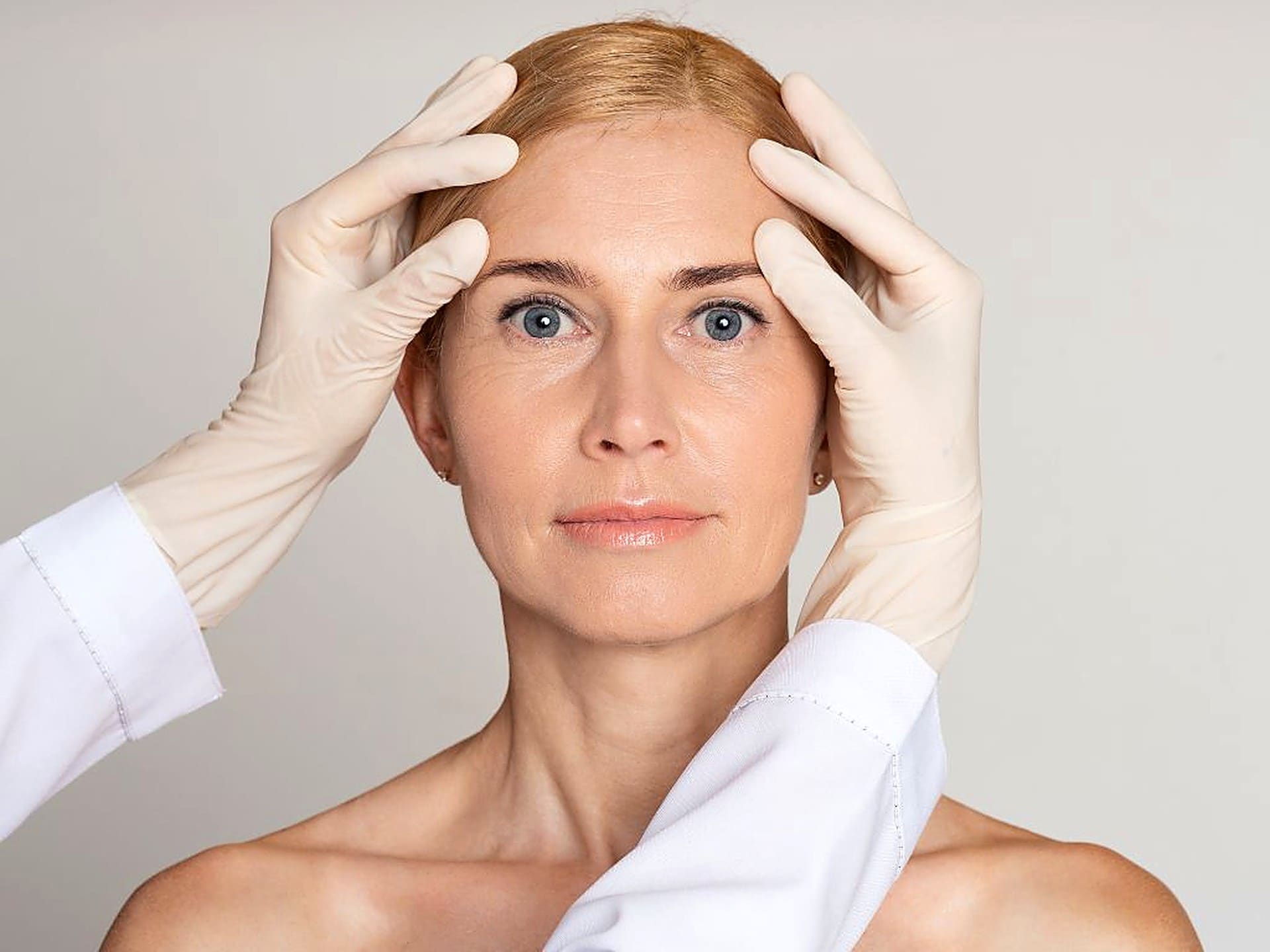 Gloved physician assessing expression lines on a woman's forehead and glabella